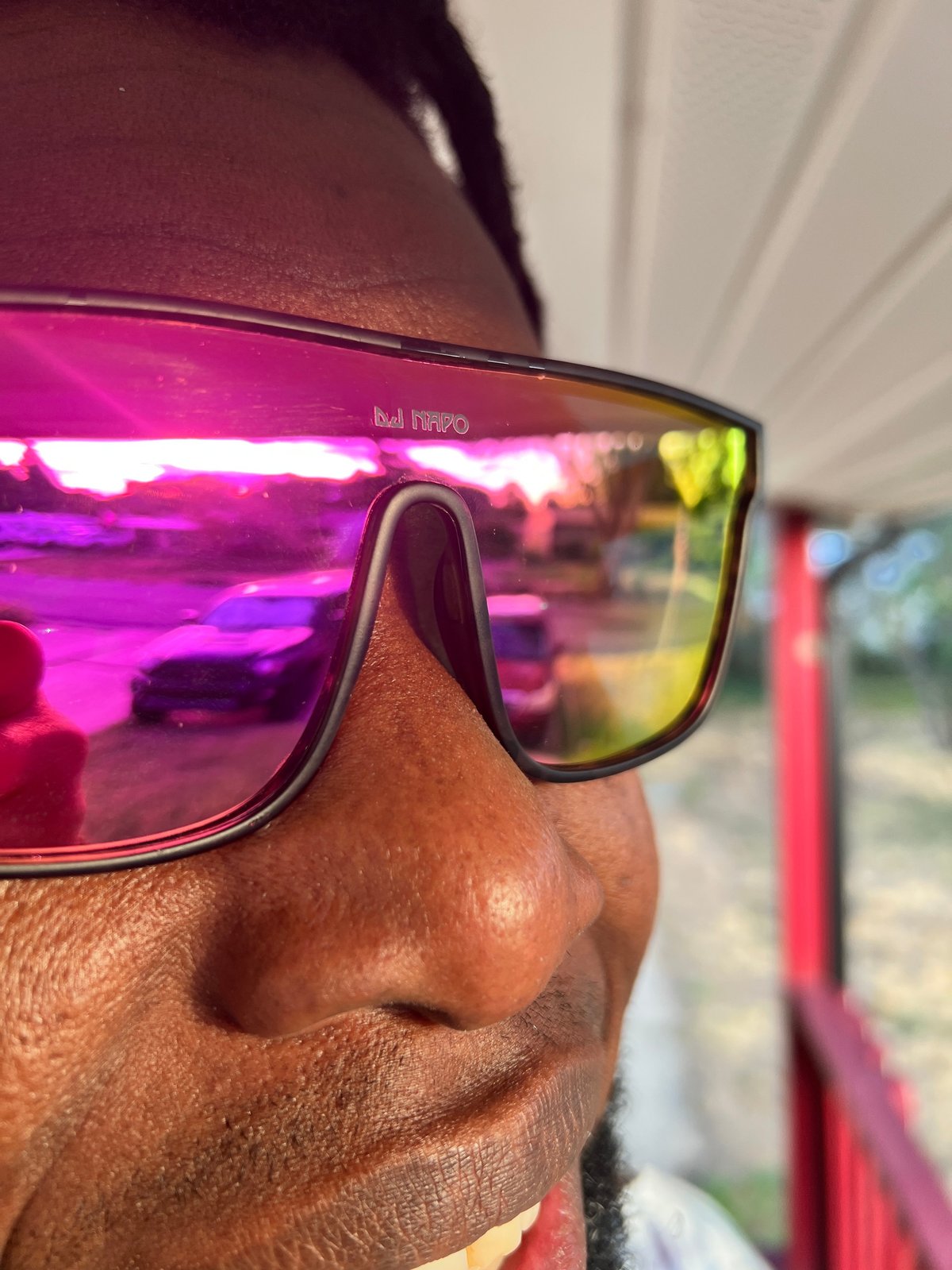 Person wearing mirrored sunglasses with bright pink and yellow reflections, outdoors with blurred background