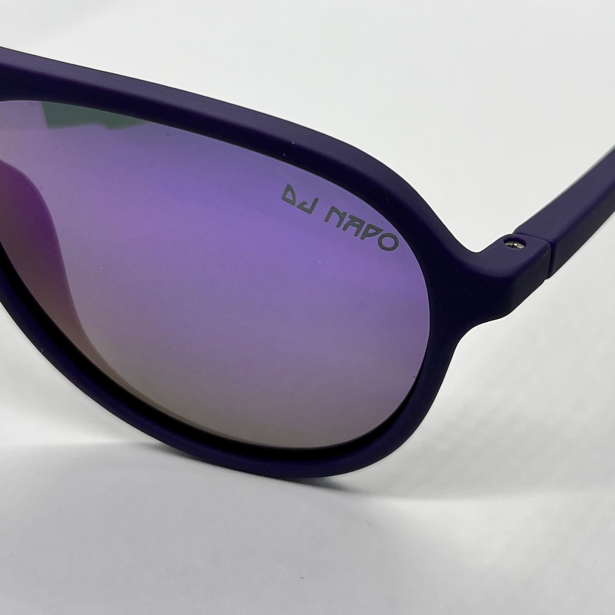 Black sunglasses with purple-tinted lenses on white background, DJ Napo branding visible on lens