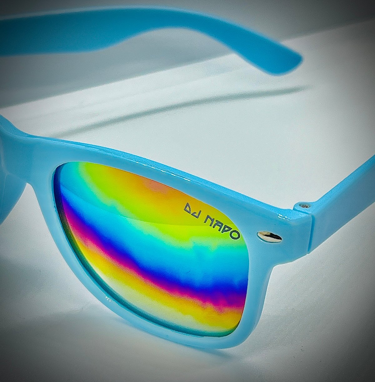 Light blue sunglasses with rainbow-colored gradient lenses and DJ Nappo branding on the frame