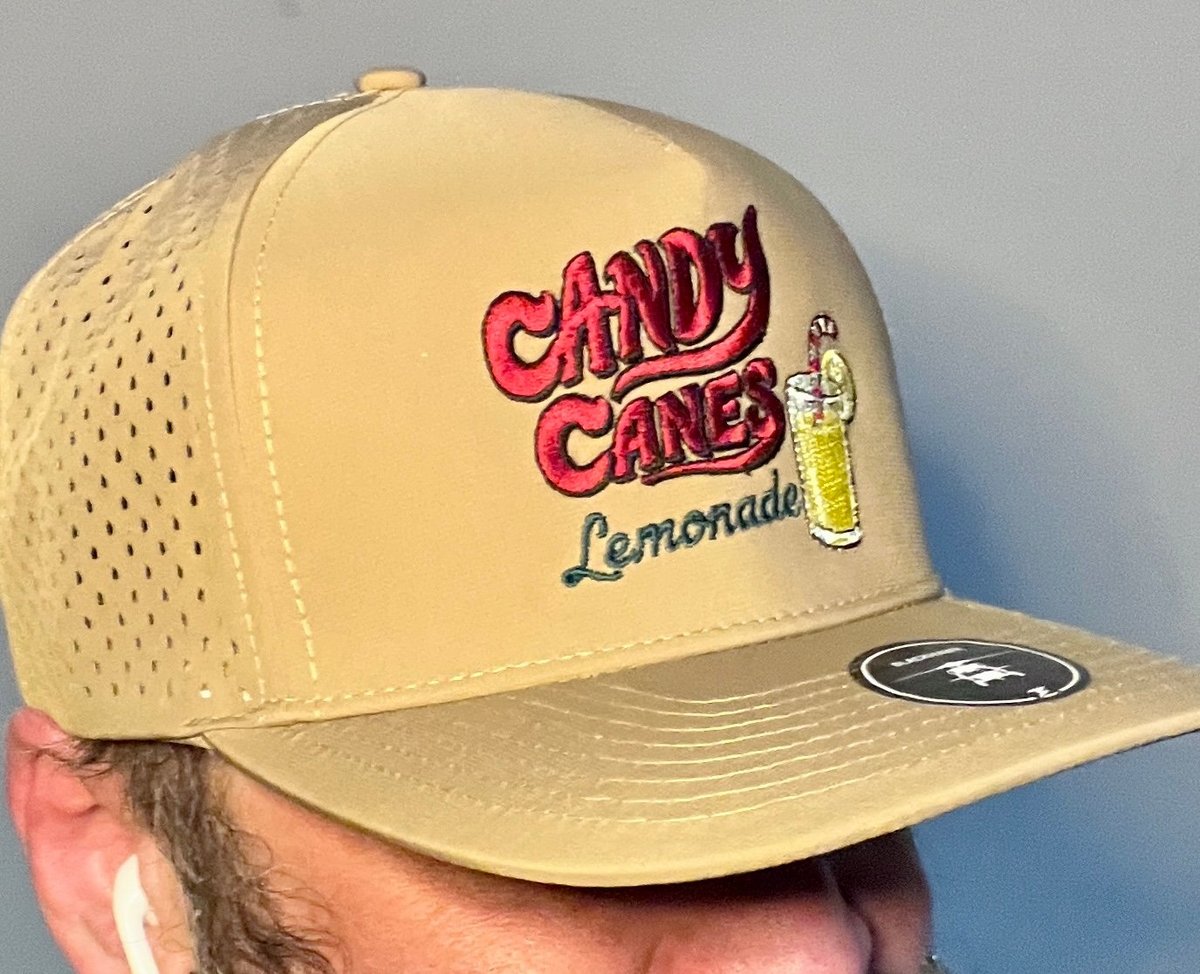 Yellow baseball cap with Candy Cane Lemonade graphic and mesh back panel, held in hand