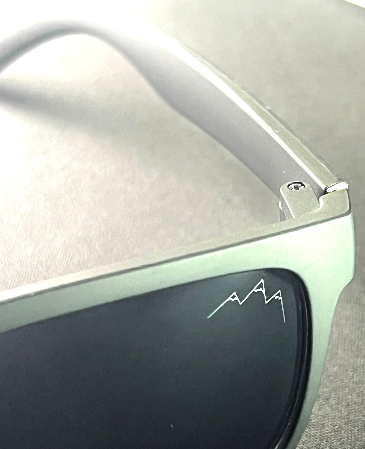 Mint green sunglasses with white frames and the TLA mountain logo etched on the dark lens