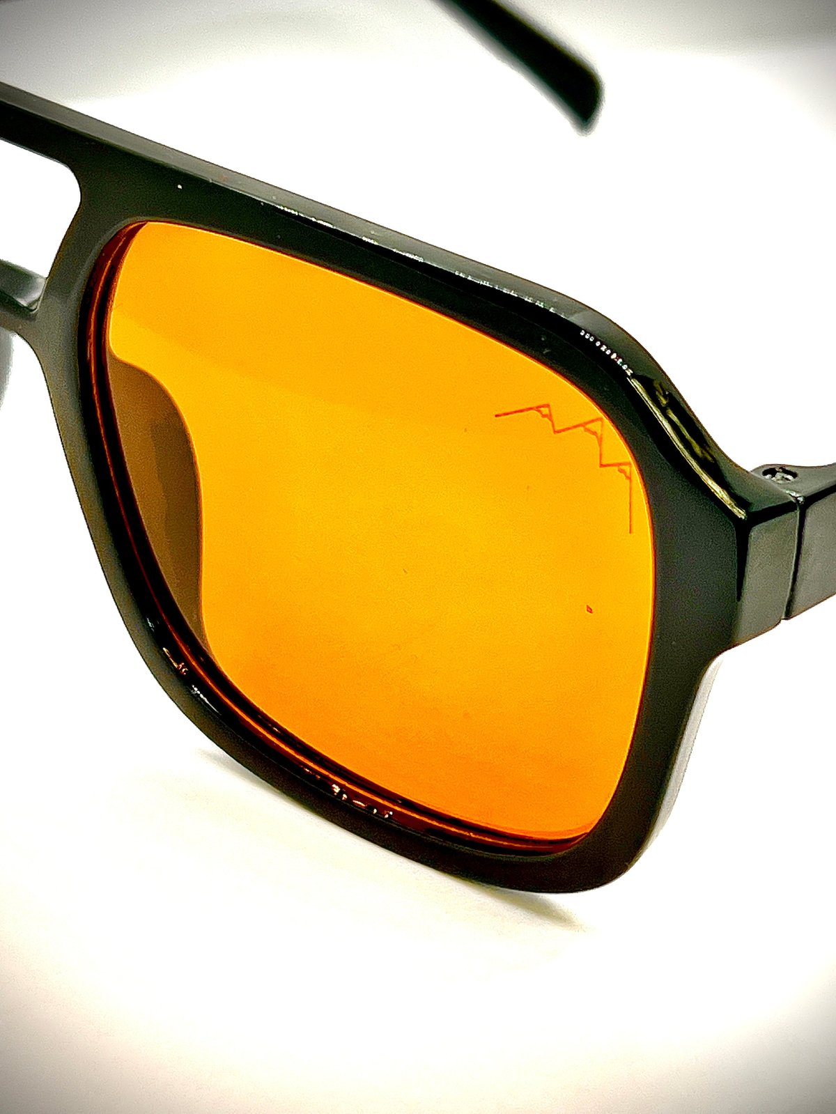 Black-framed Marty sunglasses with large orange amber tinted square lenses, the TLA mountain logo etched on the lens