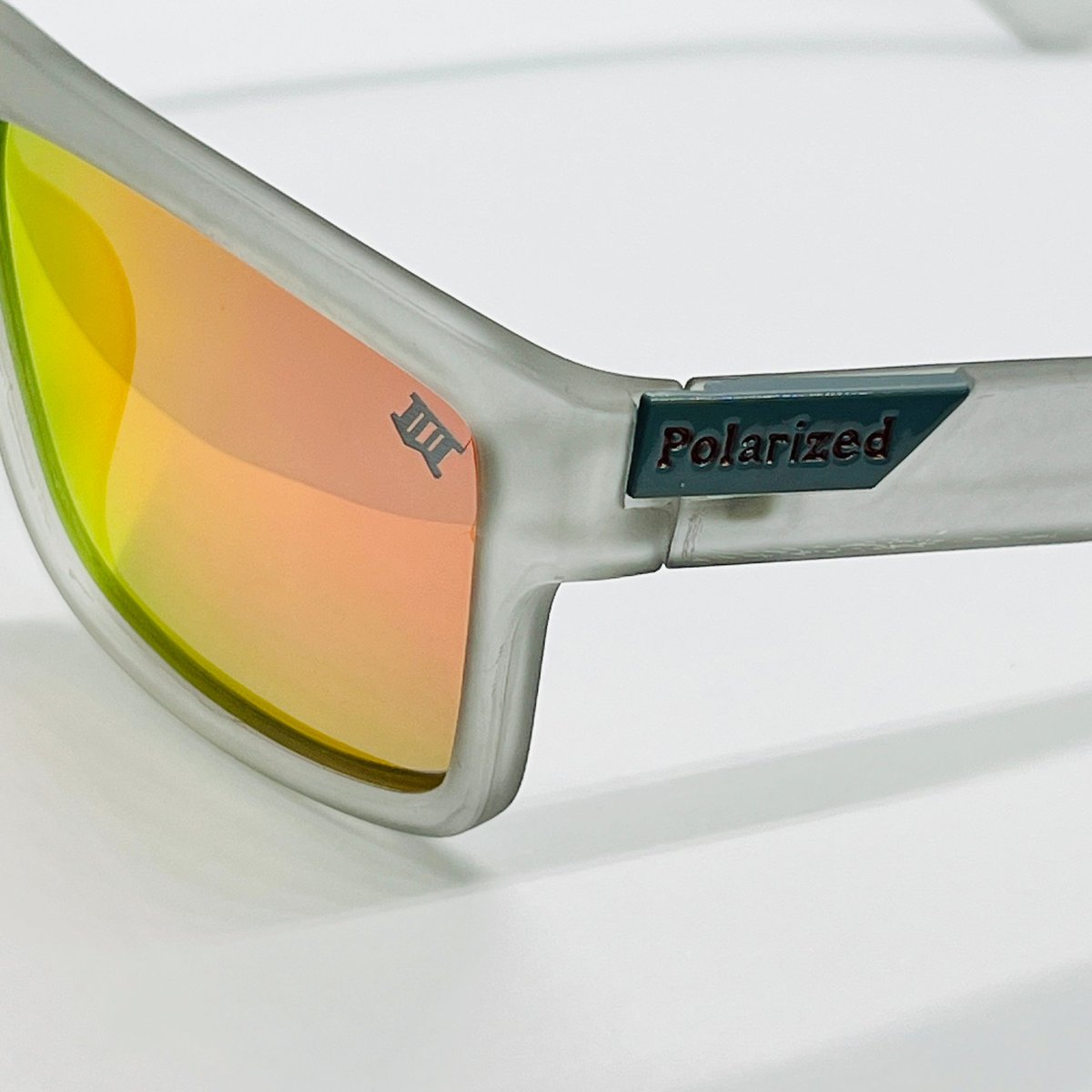 Smoke frame sunglasses with a bright red lens, with a small building icon etched onto the lens