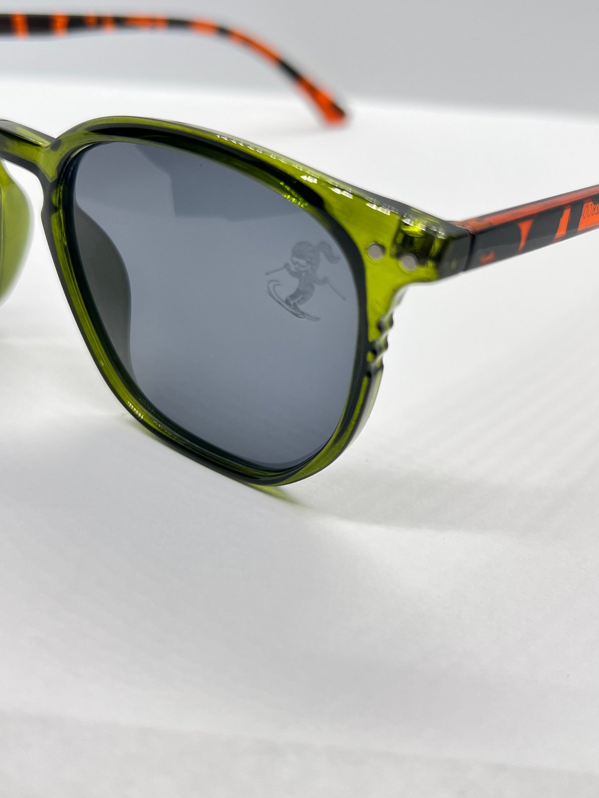 Pair of sunglasses with lime green round frames and dark tinted lenses, featuring orange and black patterned temple arms